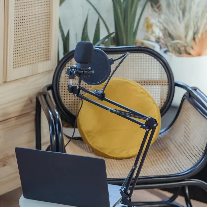 Micrófono y laptop sobre escritorio con notas, mostrando planificación de ideas para podcast.